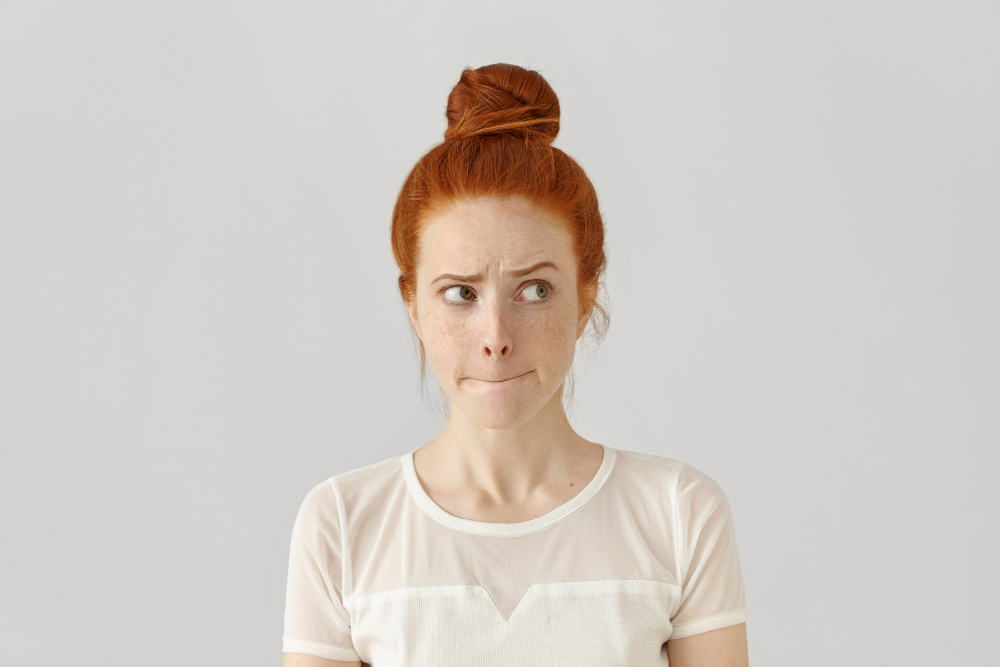 studio isolated shot of doubting confused cute young redhead freckled female looking sideways
